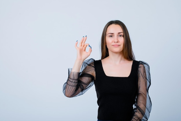 Young girl is showing okay gesture by looking at camera on white background