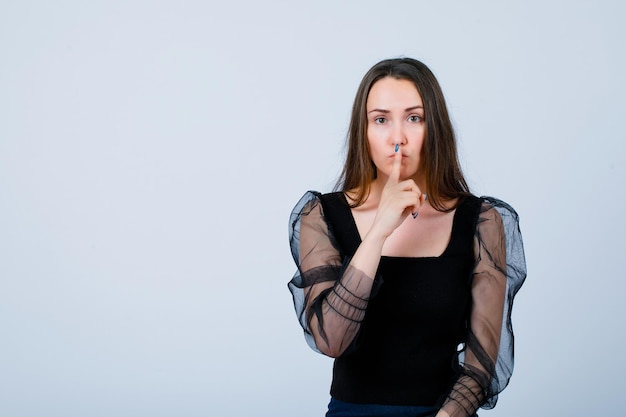 Young girl is showing silence gesture by holding forefinger on lips on white background