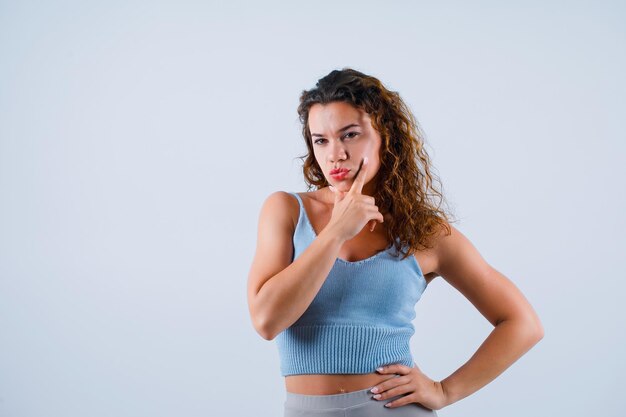 Young girl is thinking by putting hand on chin and putting other hand on waist on white background