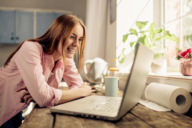 Young girl in the kitchen, smiling looking at laptop.