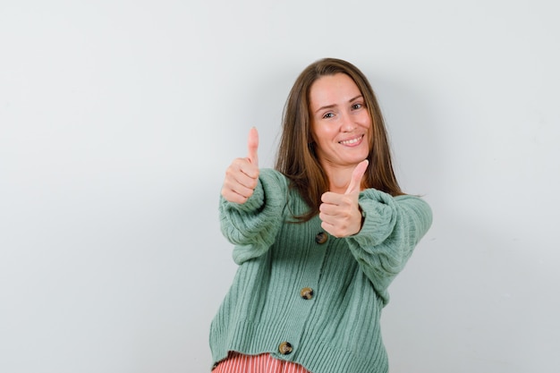 Free photo young girl in knitwear showing double thumbs up and looking happy , front view.