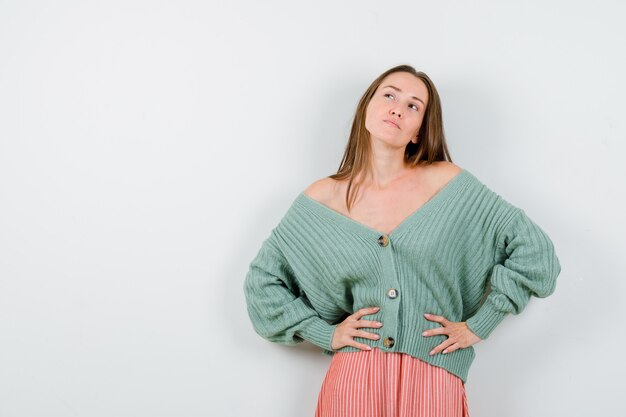 Young girl in knitwear, skirt holding hands on waist and looking happy , front view.