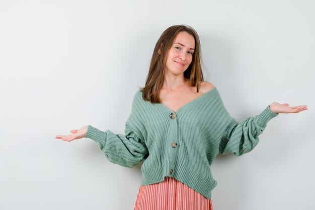 Young girl in knitwear, skirt showing helpless gesture and looking happy , front view.