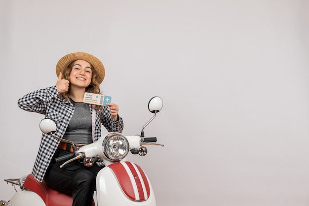 young girl on moped holding ticket giving thumbs up on grey