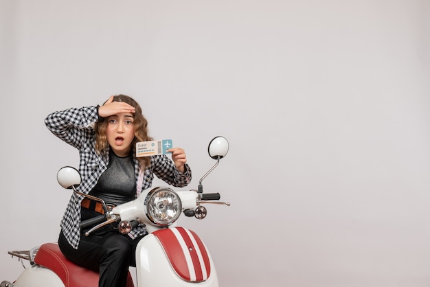 Free photo young girl on moped holding ticket looking at something on grey