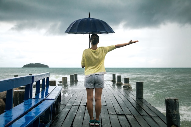 Free photo young girl on pier with umbrella stands with his back to the sea