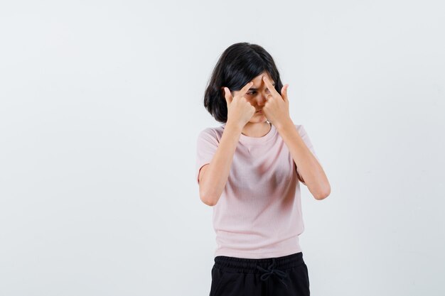 Young girl in pink t-shirt and black pants popping a pimple and looking serious