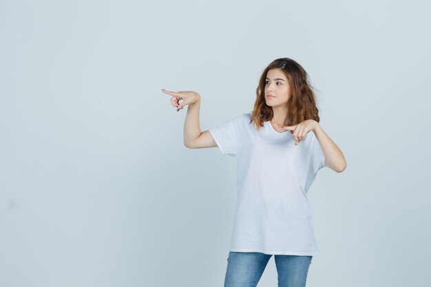 Young girl pointing to the left side in t-shirt, jeans and looking confident , front view.