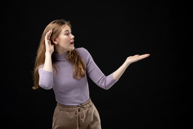 Young girl pointing something on the left side and listening carefully on dark