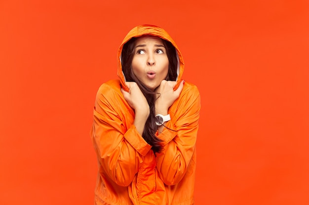 The young girl posing at studio in autumn jacket isolated on red. Human negative emotions. Concept of the cold weather. Female fashion concepts