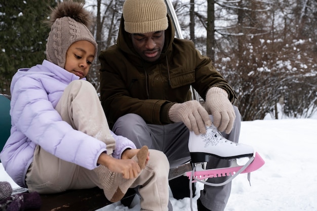 Young girl putting on her ice skates with the help of her father