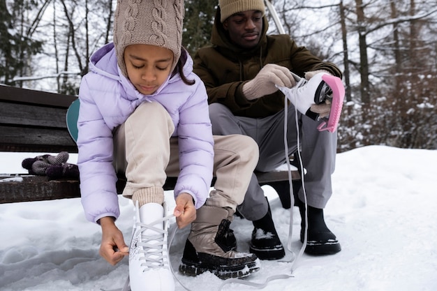 Young girl putting on her ice skates with the help of her father