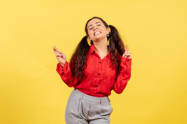 young girl in red blouse crossing her fingers feeling excited on yellow