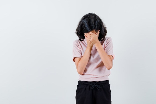 Young girl rubbing covering face with hands in pink t-shirt and black pants and looking tired