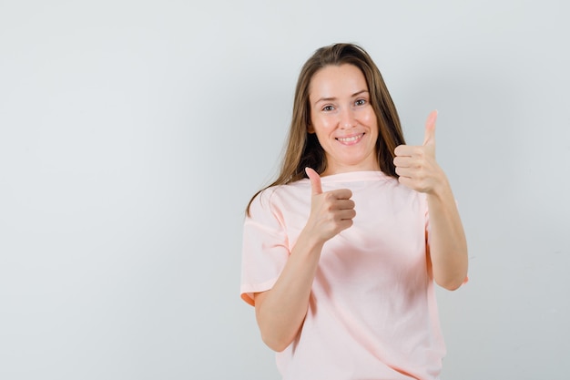 Free photo young girl showing double thumbs up in pink t-shirt and looking joyful , front view.