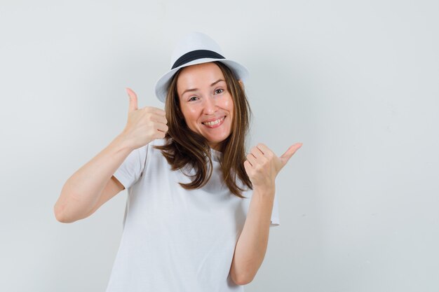 Young girl showing double thumbs up in white t-shirt, hat and looking happy , front view.