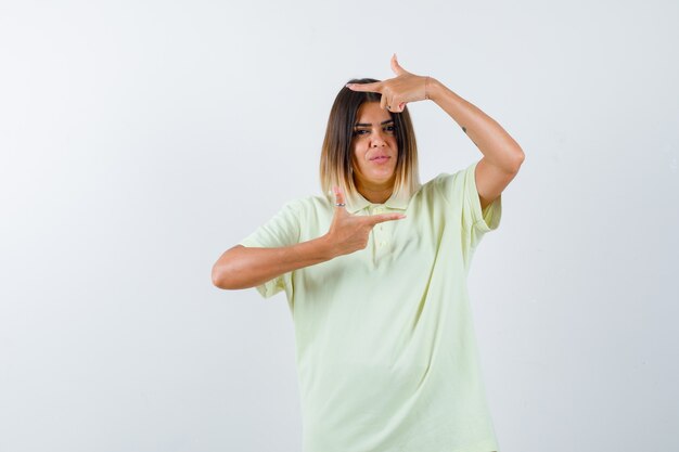 Young girl showing frame gesture in t-shirt and looking serious. front view.