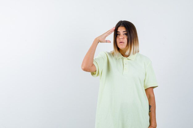 Young girl showing salute gesture in t-shirt and looking serious , front view.