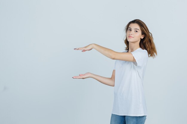 Young girl showing size sign in t-shirt, jeans and looking confident , front view.