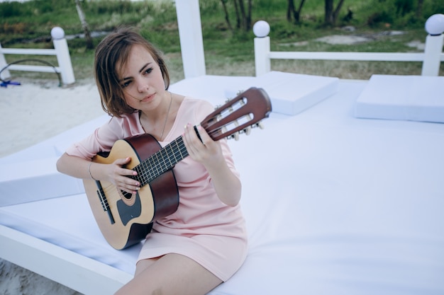 Young girl sitting on a bed playing the guitar