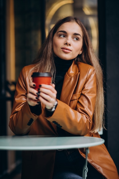 Young girl sitting outside the cafe and drinking coffee