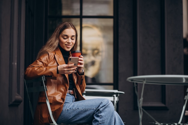 Young girl sitting outside the cafe and drinking coffee