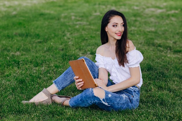 Young girl sitting in a park with a tablet in hands and looking to the side