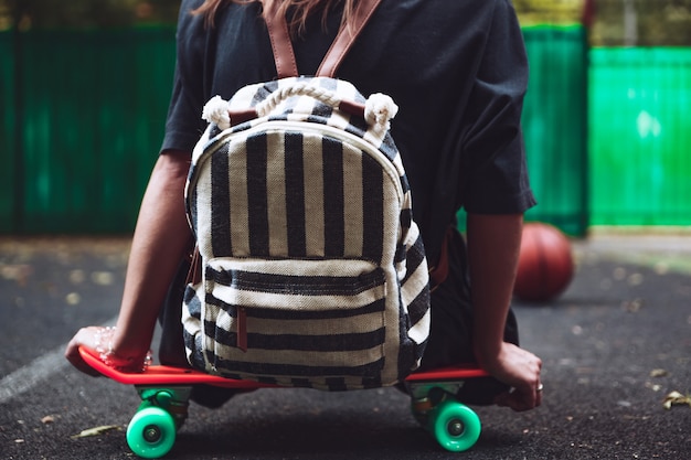 Free Photo young girl sitting on plastic orange penny shortboard on asphalt in cap