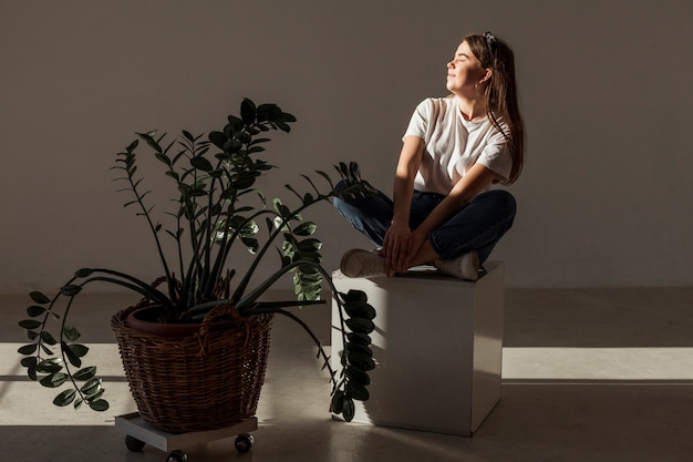 Free photo young girl sitting in the shadows and plant