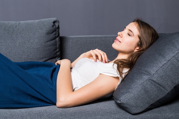 Young girl sleeping on a sofa covered with blue coverlet on gray background