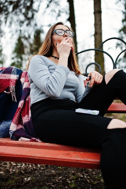 Young girl smoking cigarette outdoors sitting on bench Concept of nicotine addiction by teenagers