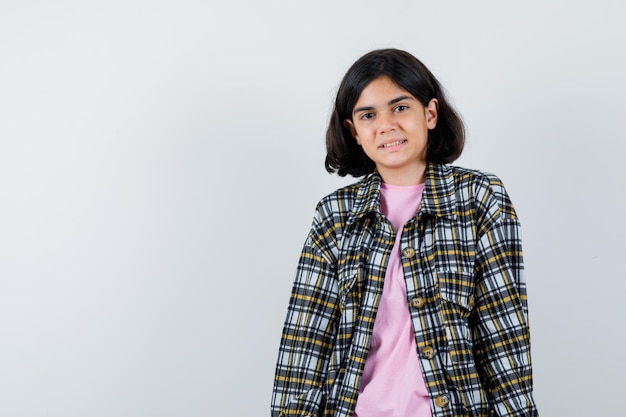 Free photo young girl standing straight, smiling and posing at camera in checked shirt and pink t-shirt and looking happy