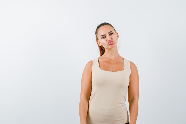 Free photo young girl standing straight while posing, sending kisses in beige top, black pants and looking confident , front view.