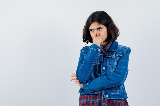 Young girl standing in thinking pose in checked shirt and jean jacket and looking pensive. front view.