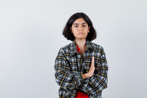 Young girl stretching hand to stop in checked shirt and red t-shirt and looking serious , front view.