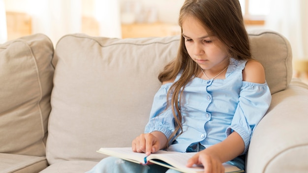 Free photo young girl studying at home  on couch with copy space