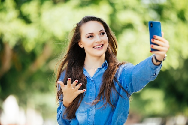 Young girl take selfie from hands with phone on summer city street. Urban life concept.