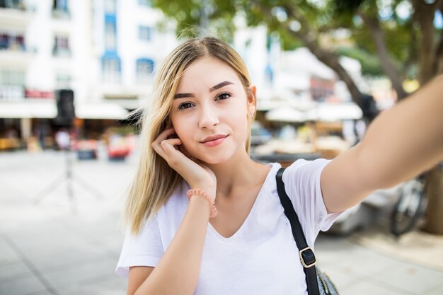 Young girl take selfie from hands with phone on summer city street.