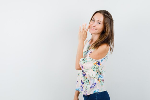 Young girl telling secret behind hand in shirt, jeans and looking joyful.