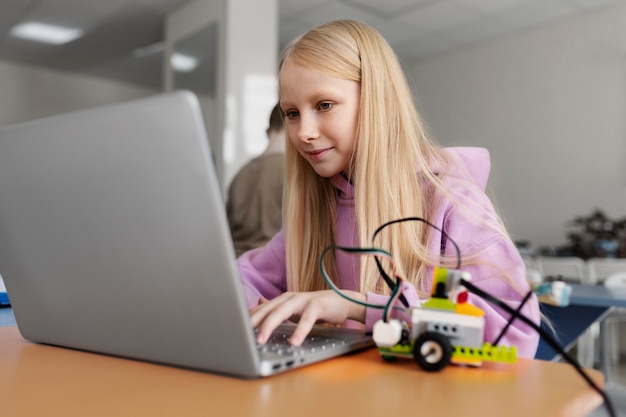 Free photo young girl using a laptop and electronic parts to build a robot