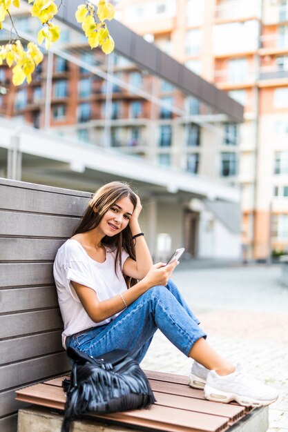 Young girl using a smart phone and texting sitting in a bench of an urban park