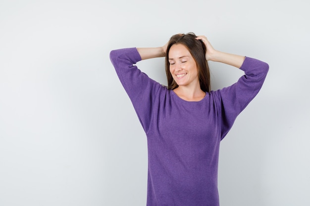 Young girl in violet shirt posing with raised hands on head and looking attractive , front view.