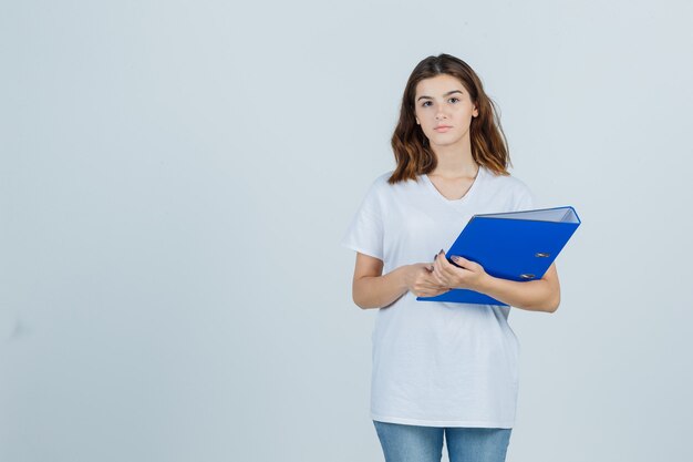 Young girl in white t-shirt holding folder and looking sensible , front view.