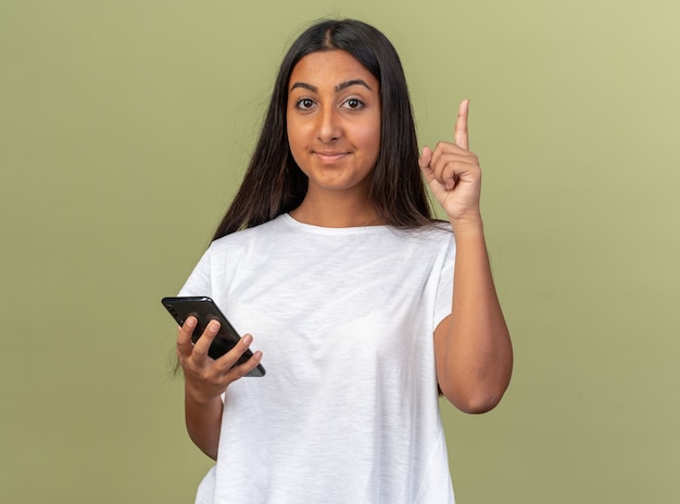 Young girl in white t-shirt holding smartphone looking at camera with smile on smart face