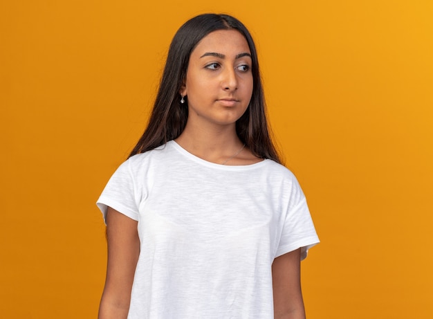 Young girl in white t-shirt looking aside with serious confident expression standing over orange