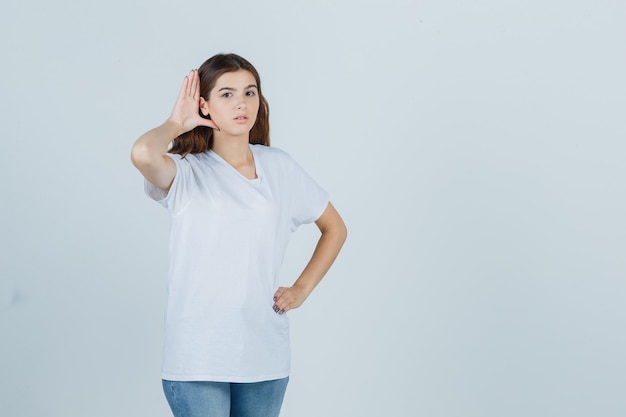 Young girl in white t-shirt overhearing private conversation and looking curious , front view.