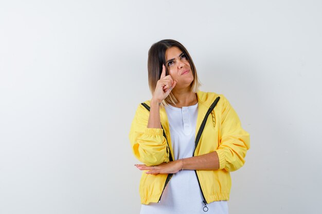 Young girl in white t-shirt , yellow jacket raising index finger in eureka gesture and looking sensible , front view.