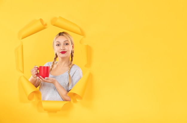 Free photo young girl with cup of tea on the torn yellow paper background facial advertising shopping