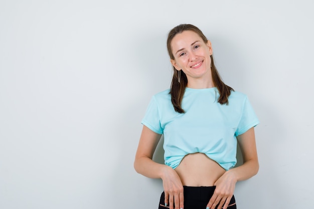 Free photo young girl with hands on waist in turquoise t-shirt, pants and looking glad , front view.