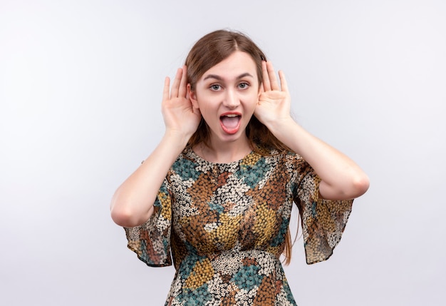 Young girl with long hair wearing colorful dress having fun imitating big ears with arms 